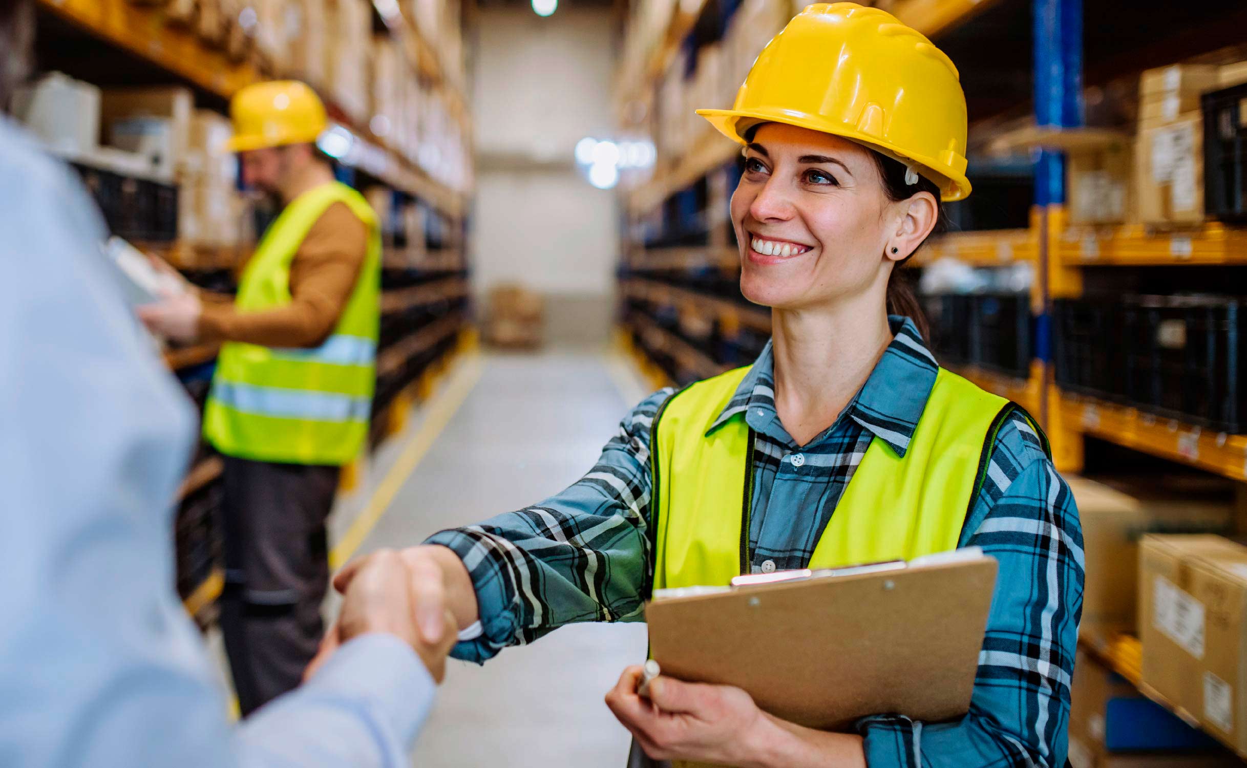 A female warehouse manager smiling and shaking hands with a new hire